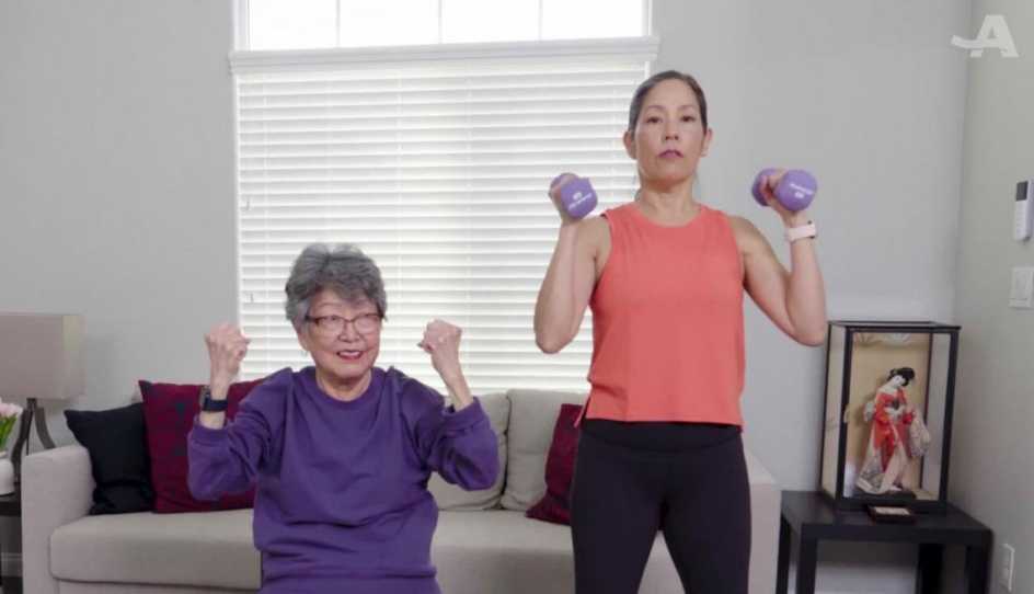 A woman sitting in a chair, another woman standing with dumbbells in her hands.