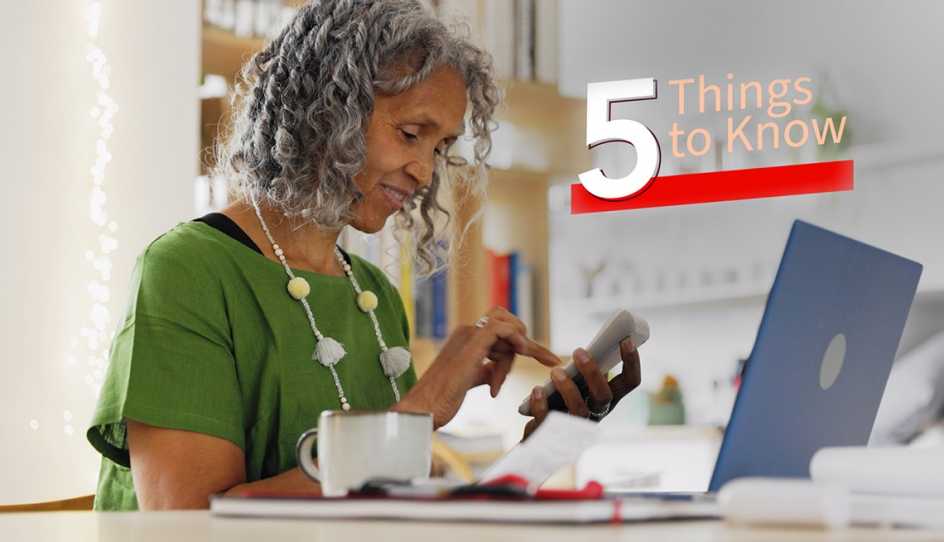 a woman is looking at her phone with her laptop on a desk