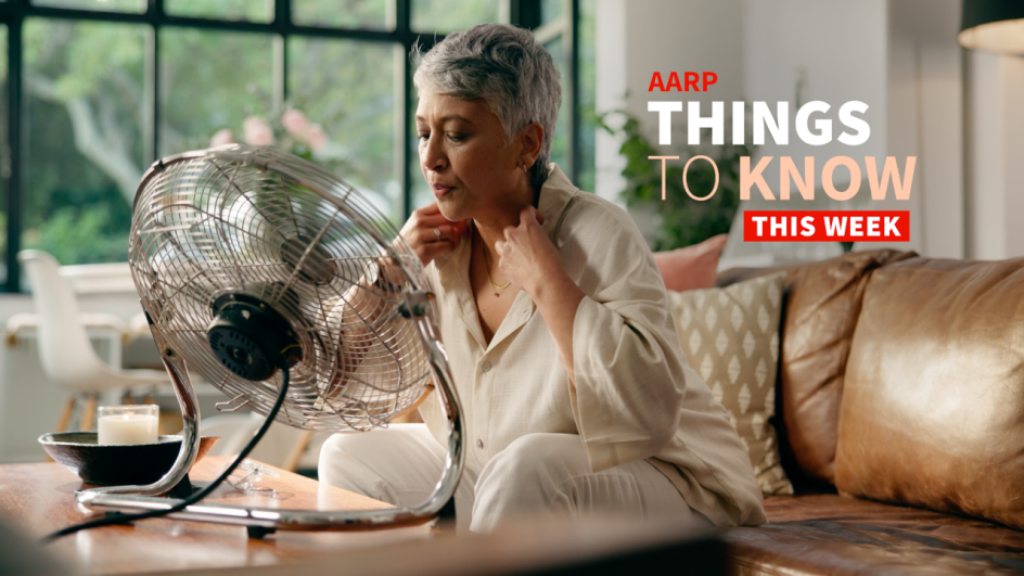 An older adult woman sitting on a leather couch tries to keep cool in front of a metal fan.