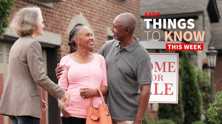 a photo shows a couple embracing with a realtor outside a house with a home for sale sign