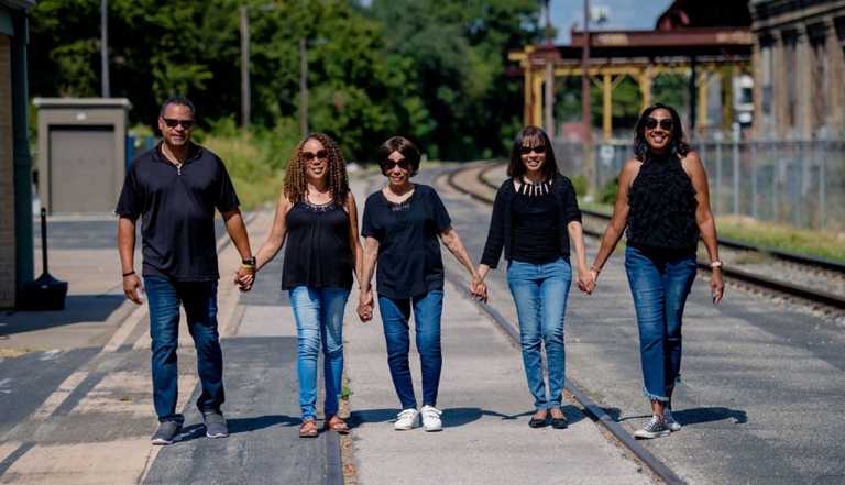 a family walks together along train tracks, smiling and holding hands