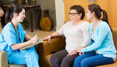 A female medical professional taking notes while talking with a Hispanic woman and her adult daughter