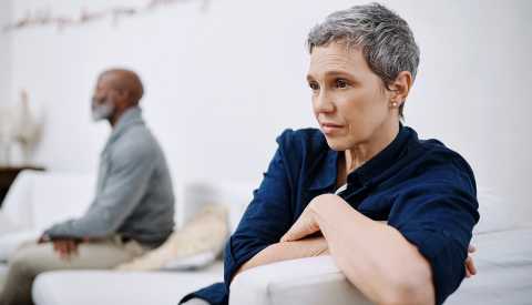 an upset looking woman sitting on the other end of the couch from her husband