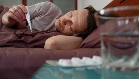 Mature woman holding a thermometer and checking temperature while lying in bed