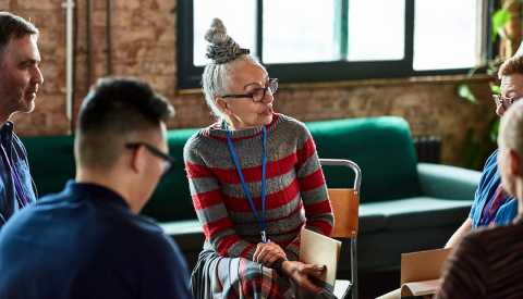 a woman sits in a meeting surrounded by people