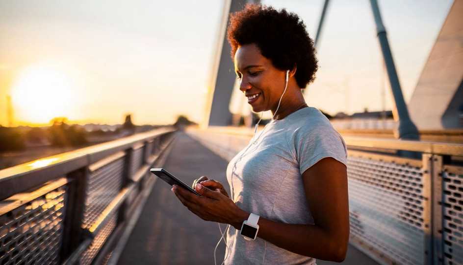 woman outside on bridge smiling looking down at phone with headphones on