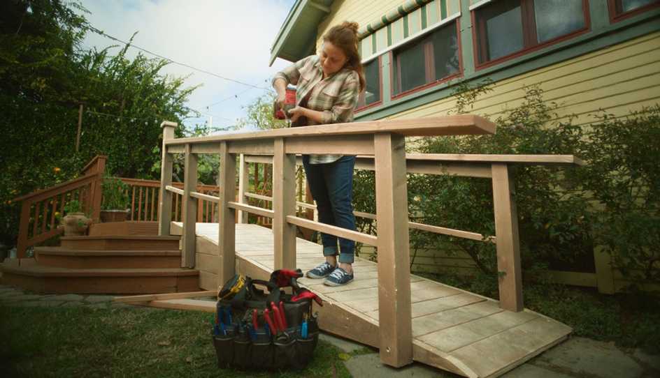 young woman outside working on a wood rail for a ramp at home, using power drill