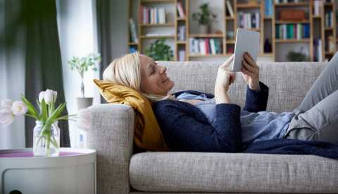 woman laying down on couch in living room looking at tablet woman laying down on couch in living room looking at tablet