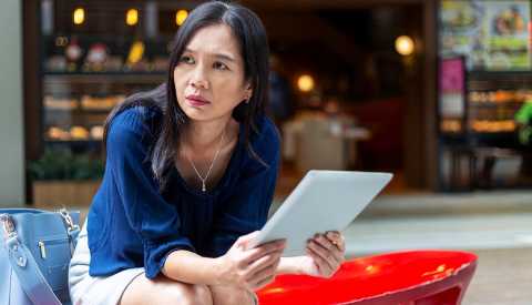 a worried woman looks at a tablet outside a retail store