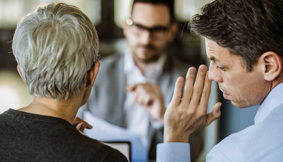 one employee whispers into another employee's ear while sitting across from a colleague