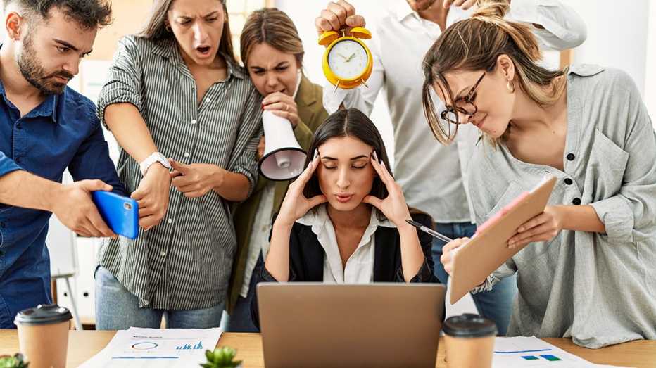 a woman in business attire tries to calm down while being surrounded by demanding co-workers