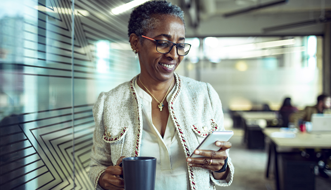 A woman looking at her phone in an office while holding a blue coffee mug