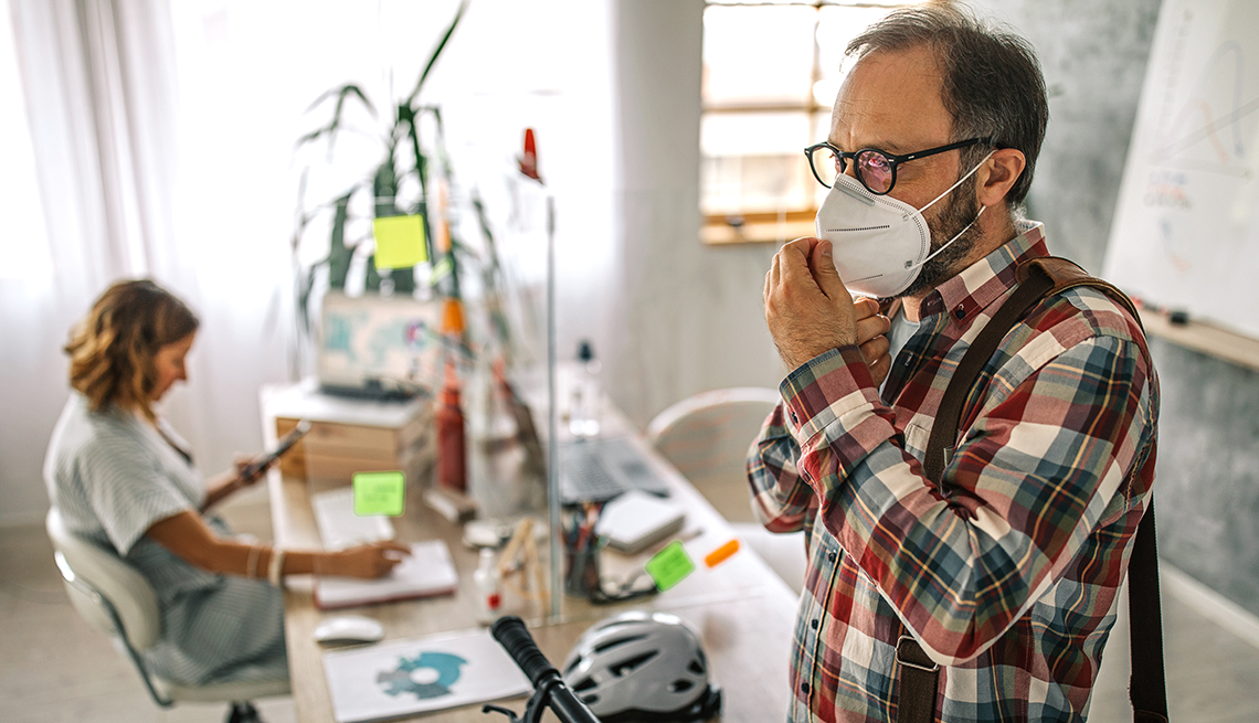 A man is standing in an office putting on a mask