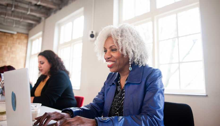  a woman in a blue jacket smiles while she works at a laptop