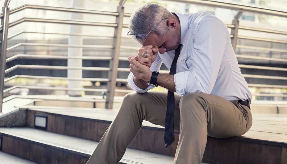 A man is sitting on steps with his head in his hands