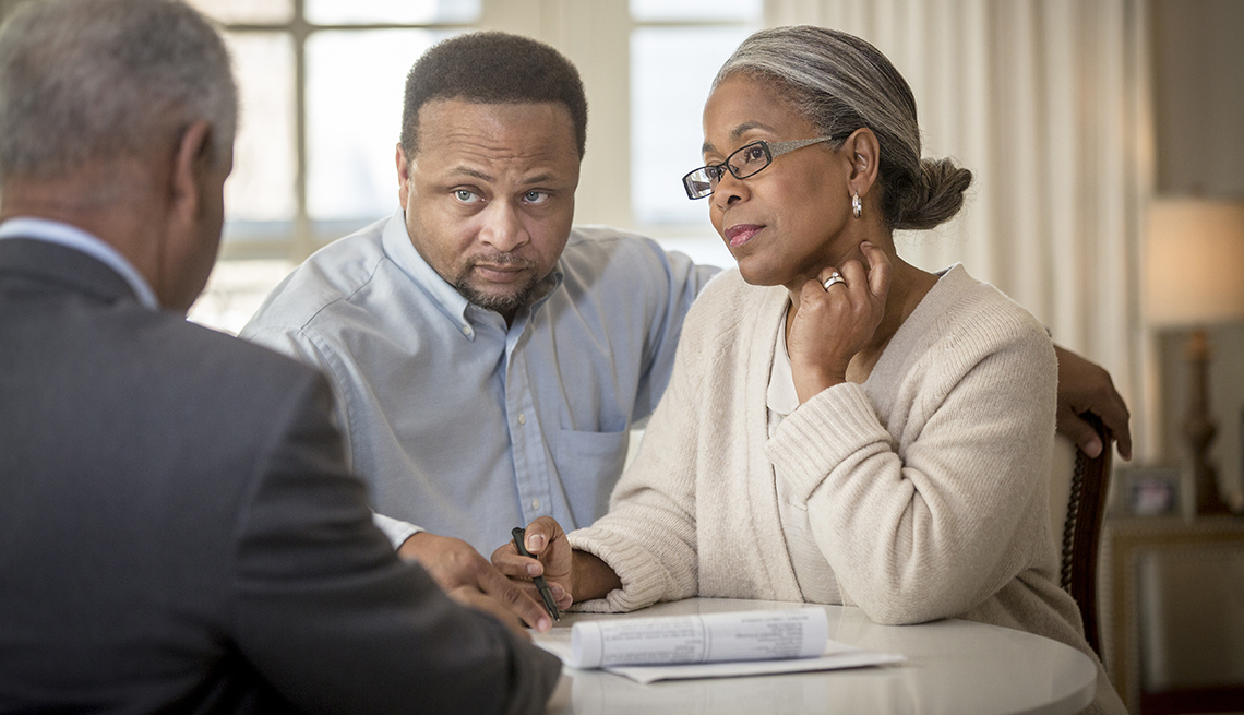 a man and woman listen to a business man while signing documents at a table