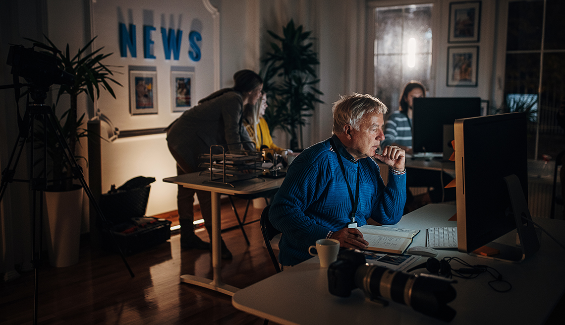 a man sits at a computer in a small newsroom at night