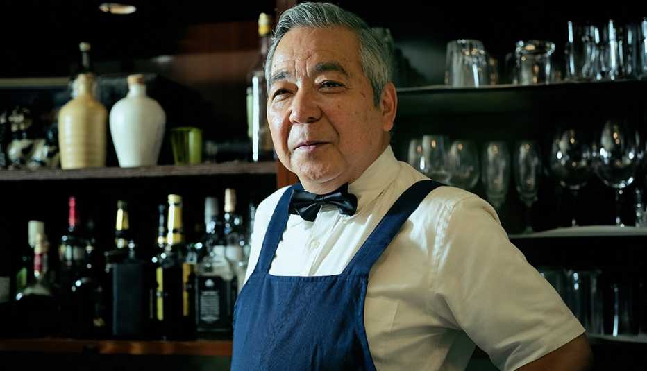 a bartender standing in front of bottless a bartender in an apron and a bowtie stands in front of bottles