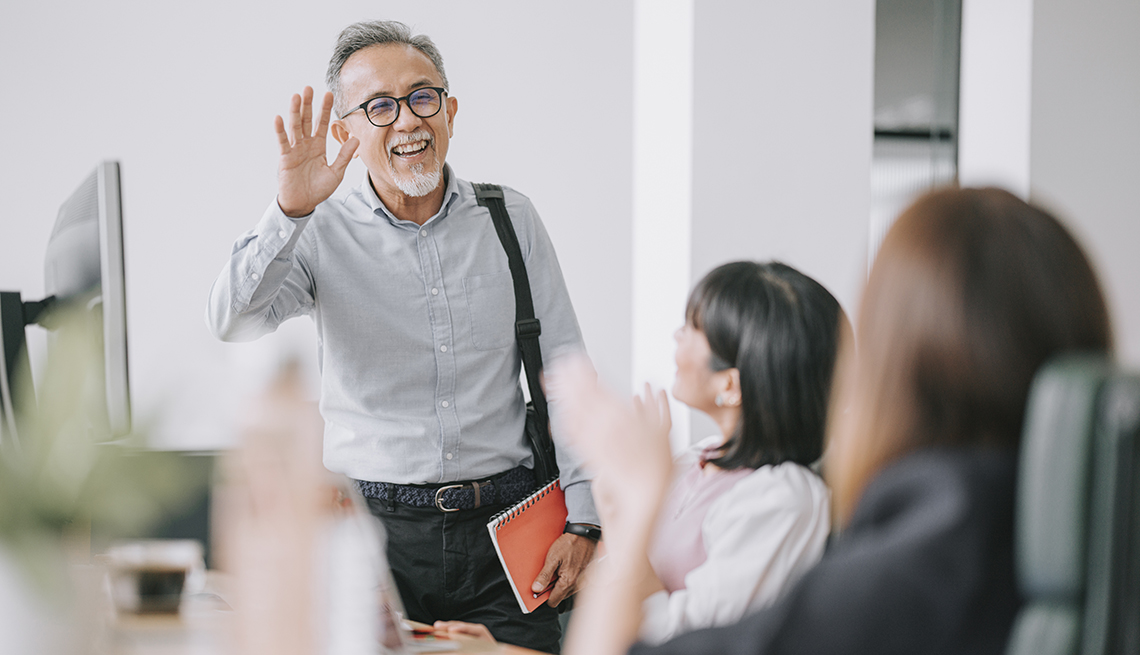 A man waves to people while walking into an office