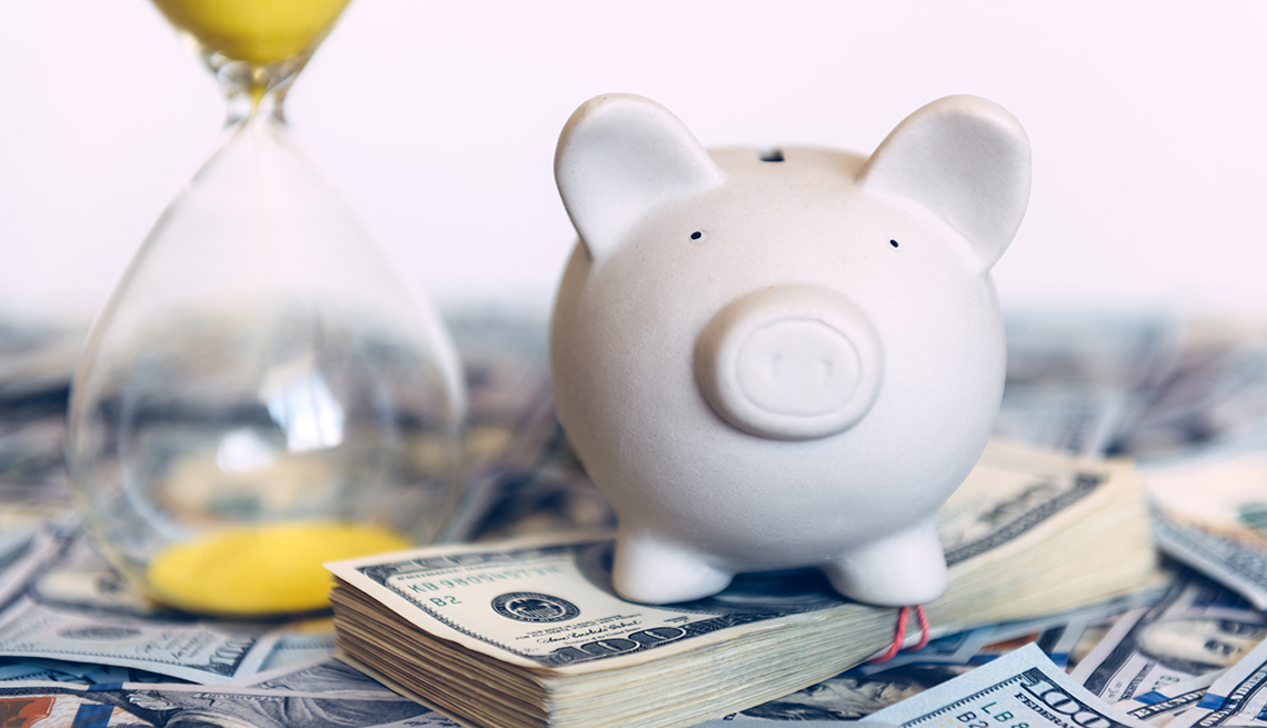 a white piggy bank on a pile of money with an hour glass