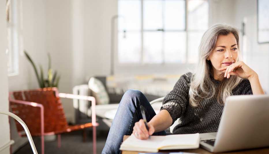 a woman writes something down while looking at a computer monitor in her home