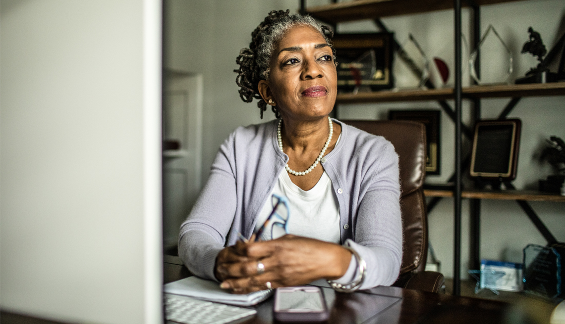 a woman sitting at a desk with a computer and a notebook looking off into the distance