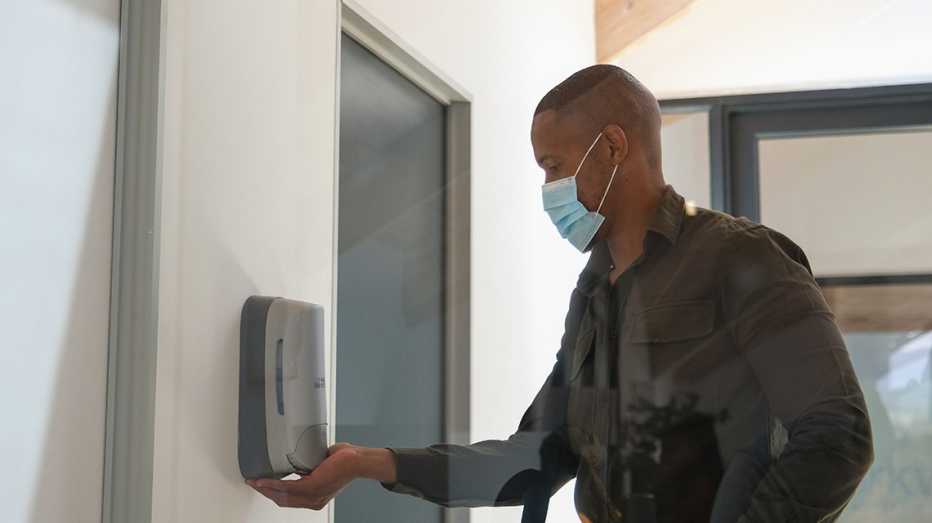 a man in a mask applies hand sanitizer before returning to work