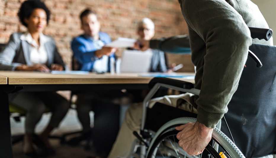a man in a wheelchair hands a piece of paper to three people a man in a wheelchair hands a resume to three people during an interview