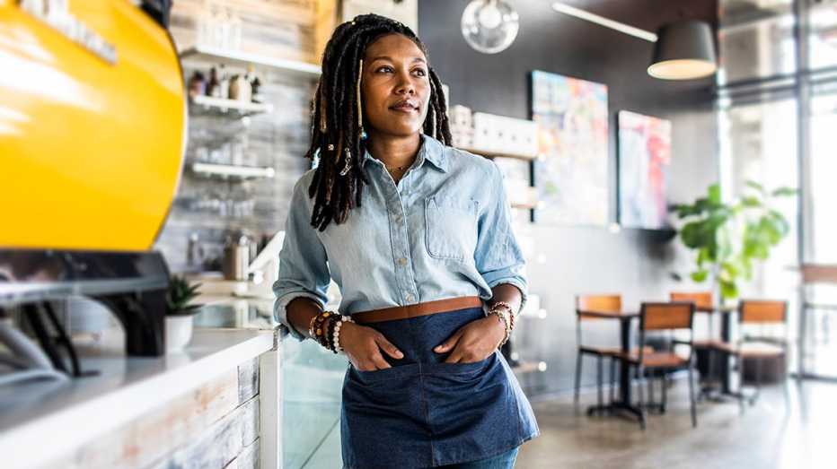 a female waitress in a casual button up shirt leans against a counter