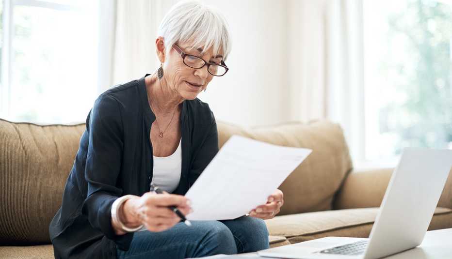 Woman looking at a paper while working on her laptop