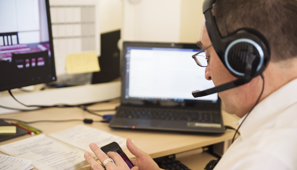 A man is looking at his phone with a headset on at a desk in his home