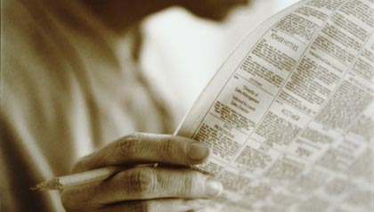 a person reading a newspaper and holding a pencil