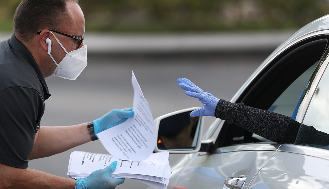 A man hands papers to someone reaching from a car window