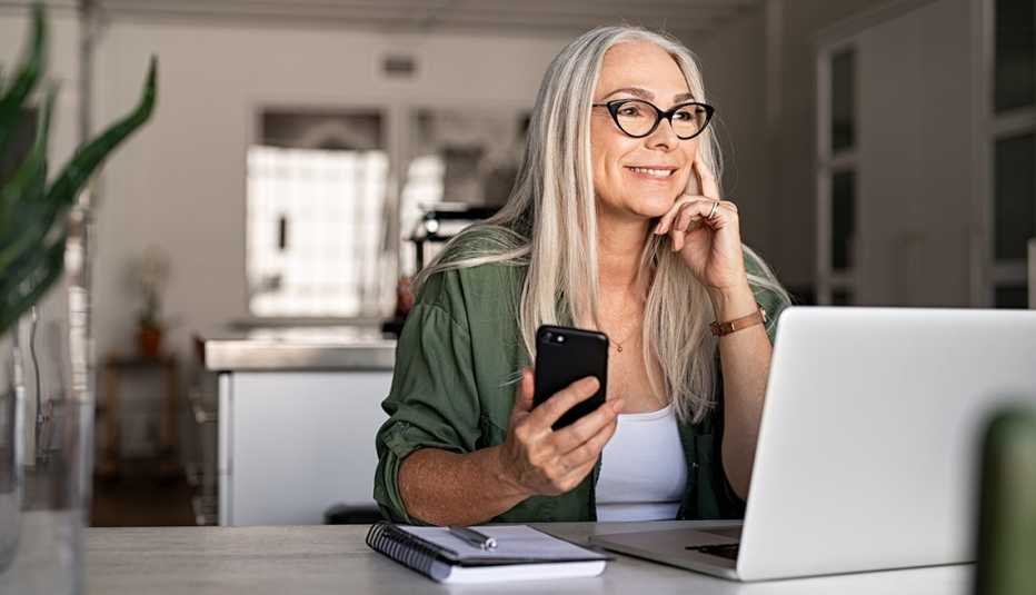 A woman is working from her desk with a phone and computer