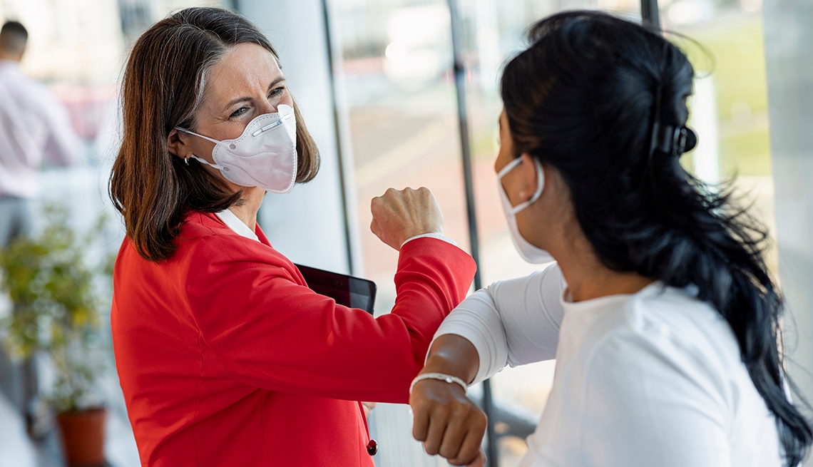two business women touch elbows while wearing masks