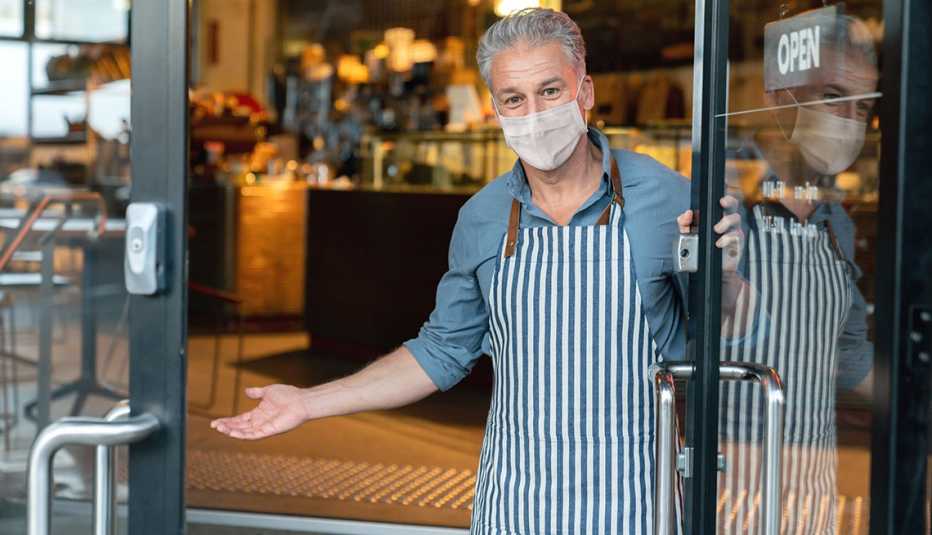 A man wearing a mask stands in a doorway of his business