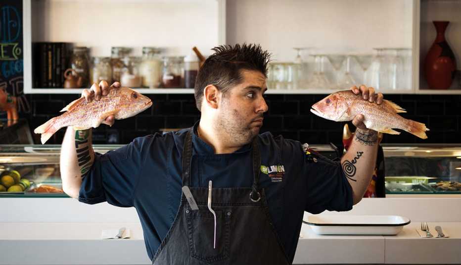 Chef Carlos Brescia sostiene dos pescados en la cocina Chef Carlos Brescia sostiene dos pescados en la cocina