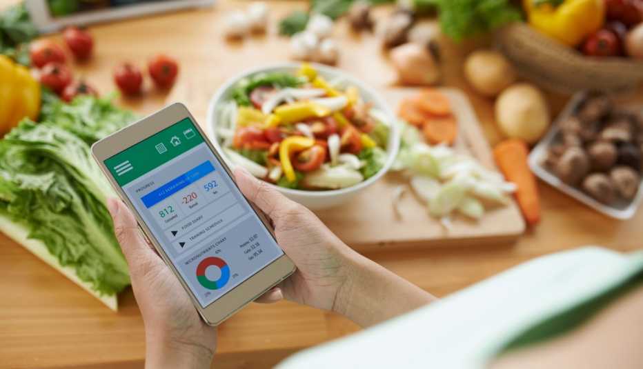Mujer usa su teléfono mientras corta vegetales Mujer usa su teléfono mientras corta vegetales