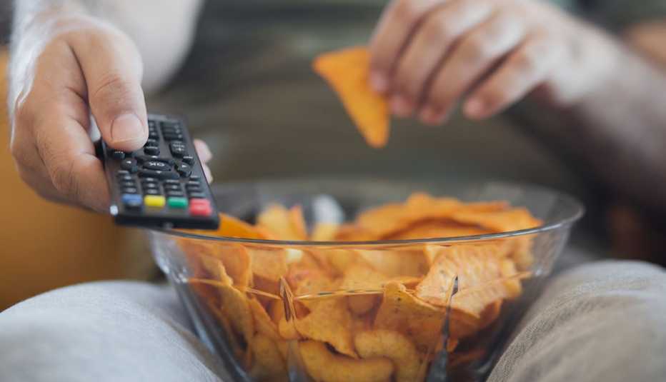 Un hombre come tortillas mientras ve televisión