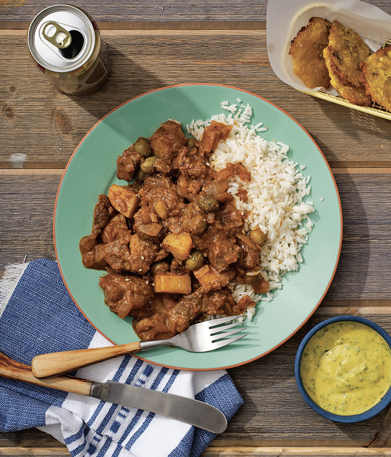 Plato servido con arroz blanco y carne guisada y salsa de mostaza y tostones por el lado