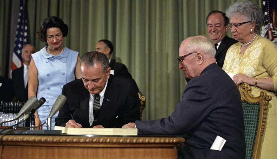 Presidente Johnson firma documento con gente congregada alrededor