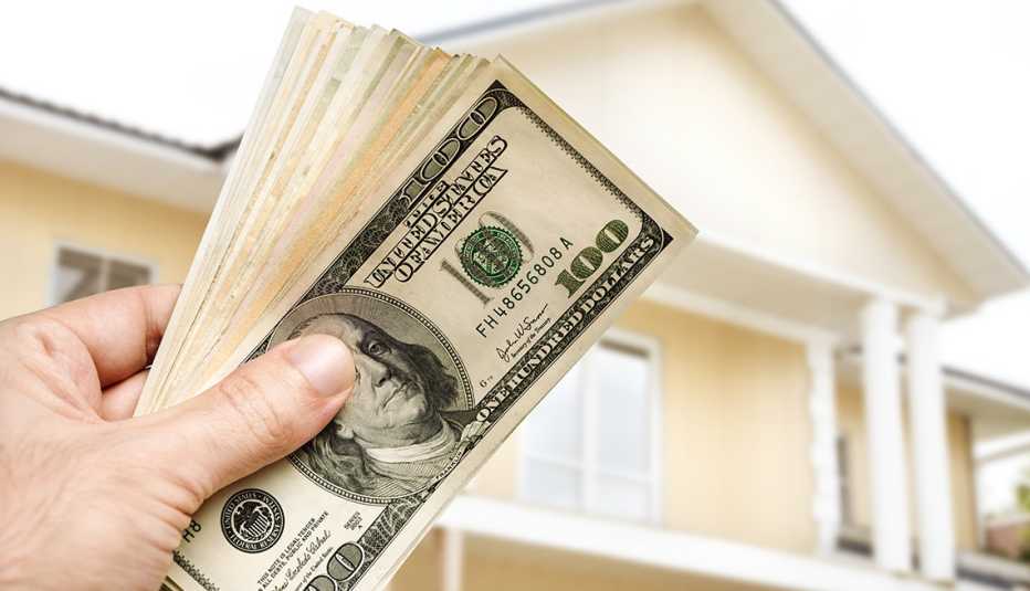 Mano sosteniendo un fajo de dólares en el exterior de una casa. Mano sosteniendo un fajo de dólares en el exterior de una casa.