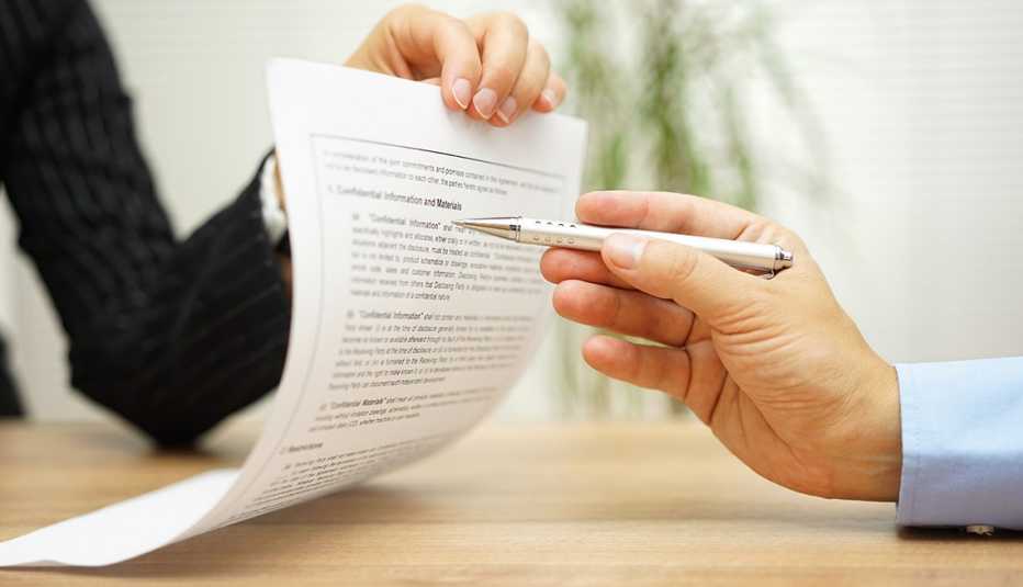 Una mano sostiene un contrato y otra lo revisa.