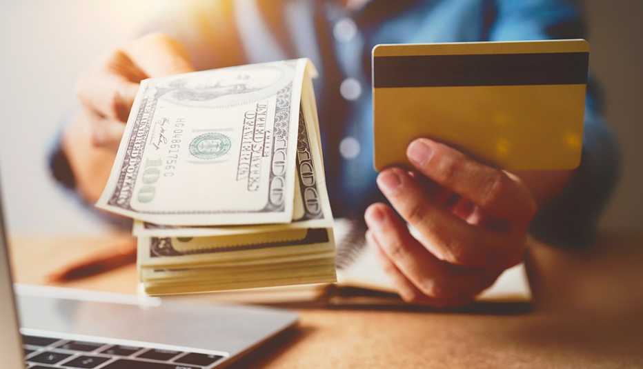 Manos frente a una computadora sostiene billetes de 100 dólares y una tarjeta de crédito. Manos frente a una computadora sostiene billetes de 100 dólares y una tarjeta de crédito.