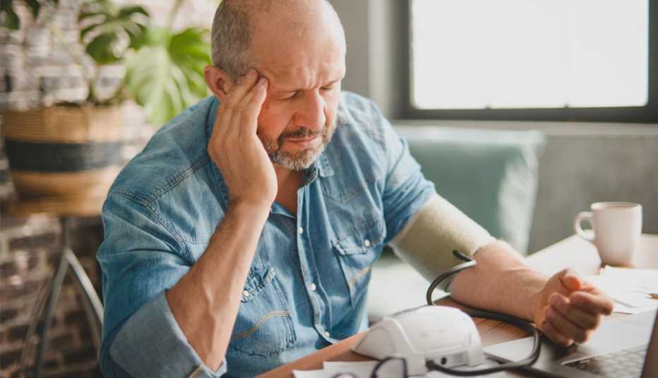 Hombre luce preocupado mientras ve sus facturas médicas y se toma la presión arterial Hombre luce preocupado mientras ve sus facturas médicas y se toma la presión arterial