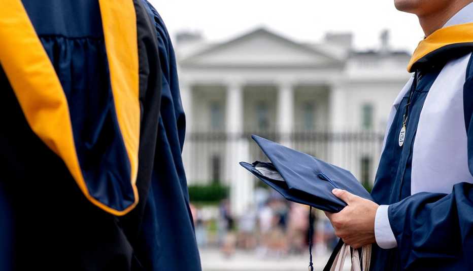 Aproximación a dos personas con toga y birrete y al fondo la Casa Blanca en Washington, DC