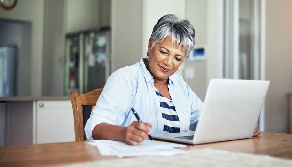Mujer en el comedor de su casa con su computadora y tomando notas. Mujer en el comedor de su casa con su computadora y tomando notas.