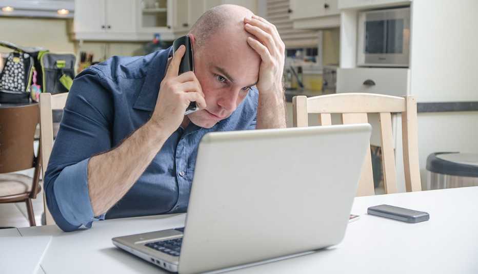 Hombre mirando su computadora mientras escucha por un teléfono