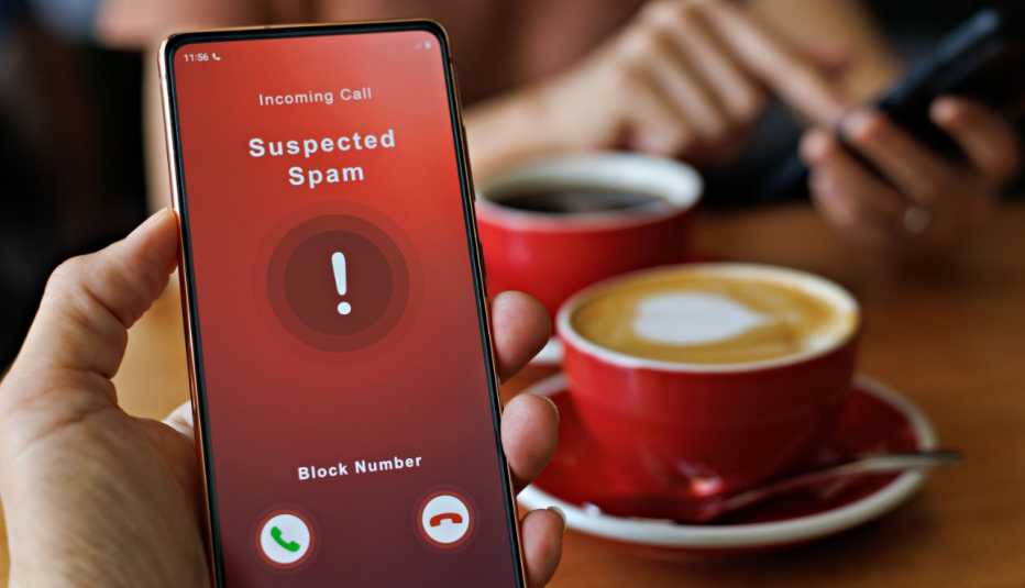 Mano de una persona sostiene un teléfono y en su pantalla ve una llamada entrante con alerta de llamada automatizada fraudulenta
