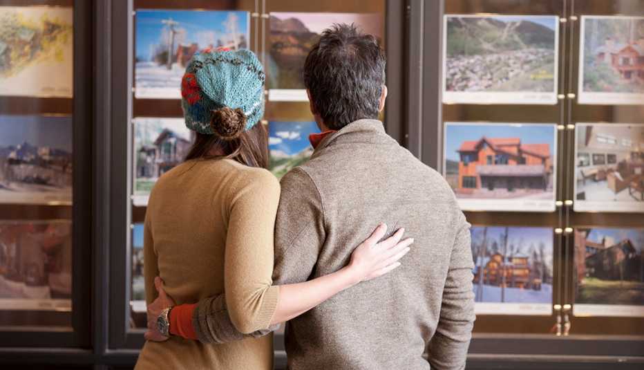 Pareja viendo opciones de viaje en fotos colgadas en un muro de una oficina de viajes.